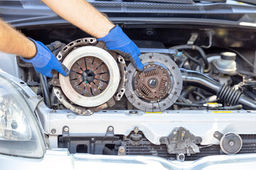 Auto mechanic holding used car pressure plate and clutch disc in front of the vehicle engine