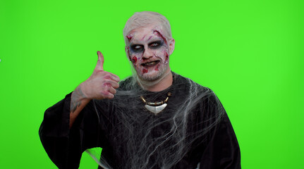 Sinister man with scary Halloween zombie makeup in costume raises thumbs up agrees with something or gives positive reply recommends advertisement likes good. Dead guy with wounded bloody scars face