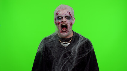Sinister man in carnival costume of Halloween crazy zombie with bloody wounded scars face screaming, shouting, trying to scare on chroma key. Horror theme of cosplay wounded undead, beast, monster