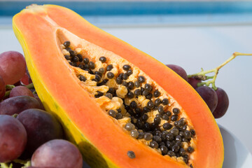 half papaya and red grapes in the mediterranean sunlight by the blue pool fruit close-up for summer holidays