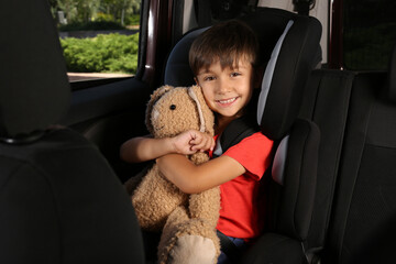 Little boy fastened with car safety belt in child seat holding toy bunny