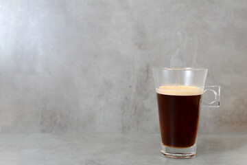 Glazed cup of steaming black coffee on gray cement-like background