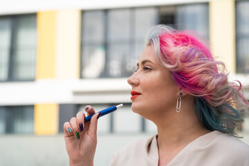 Caucasian woman with colored hair smokes an electronic cigarette.