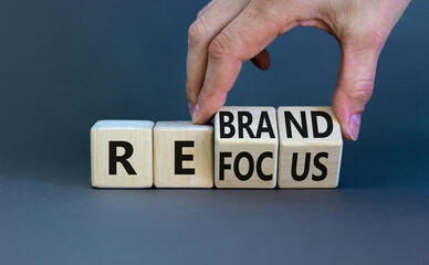 Refocus and rebrand symbol. Businessman turns cubes and changes the word 'refocus' to 'rebrand'. Beautiful grey table, grey background. Business, refocus and rebrand concept. Copy space.
