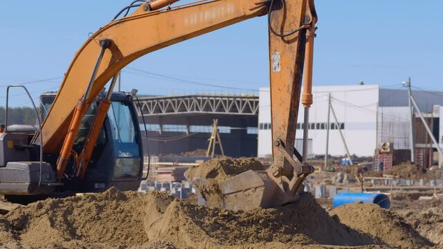 Earthwork at a construction, excavator scoop flattens large mountains of sand 