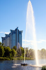 Fototapeta premium Autumn landscape of fountain in the city channel near Rusanovka neighborhood at sunny day. New high-rise fashionable houses. Concept of modern architecture from glass, steel and concrete