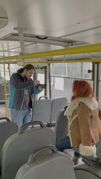 Male photographer takes picture of red-haired woman sitting at window in bus. Retro photo shoot in public transport. Girl in boho clothes. Backstage.
