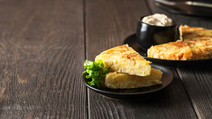 Spanish tapa.Tortilla with mayonnaise  on black plate on wooden table.Copy space