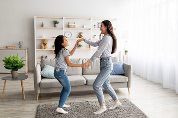Joyful asian mom and daughter dancing to music, holding hands and enjoying favorite song together...