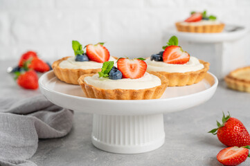 Delicious mini tarts with fresh berries and custard on a white plate on a gray concrete background. Copy space