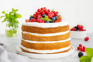 Homemade naked layered vanilla cake with whipped cream and fresh berries on top on a gray concrete...