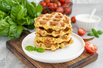 Homemade zucchini cheese waffles with sour cream and fresh basil on a plate on a gray concrete background. Vegetarian dish. Copy space.