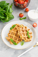 Homemade zucchini cheese waffles with sour cream and fresh basil on a plate on a gray concrete background. Vegetarian dish. Copy space.
