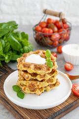 Homemade zucchini cheese waffles with sour cream and fresh basil on a plate on a gray concrete background. Vegetarian dish. Copy space.