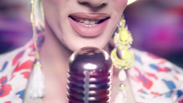 close-up of lips. male travesty artist singing into microphone on stage in safita light.
