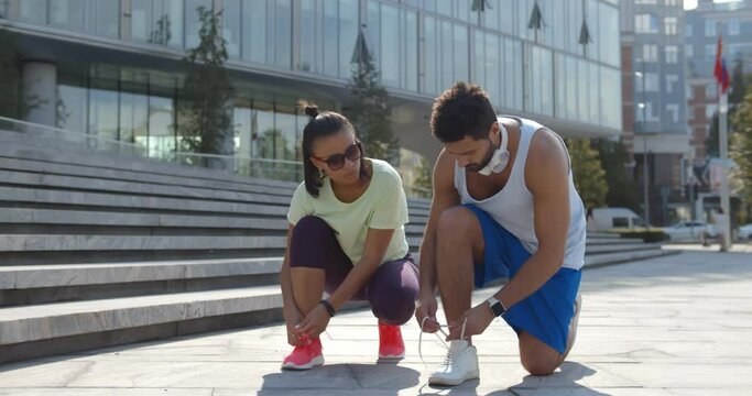 Diverse couple lacing shoes before training outdoors