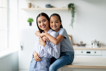 Tenderness and motherhood concept. Cute asian girl hugging mother from the back, sitting on dinner...