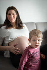 Mujer embarazada sonriente mostrando su panza y jugando con su hijo