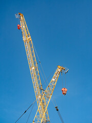 Baukräne bei klarem Himmel auf einer Baustelle. Zwei Kranarme kreuzen sich.