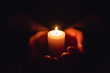 Hands holding burning candle in dark like a heart.Selective focus,black background. - Powered by Adobe