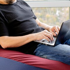 Naklejka premium Young man working with laptop sitting near panoramic windows