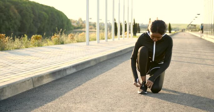 African American fit woman tiying shoelaces outdoors