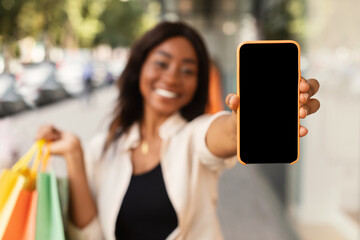 Black woman showing empty smartphone screen holding bags