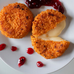 Breaded baked camembert and lingonberry sauce on a white plate.