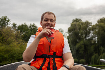 Fisherman in life jacket on a boat. Adult man drinking coffee and smiling on a boat wearing orange...