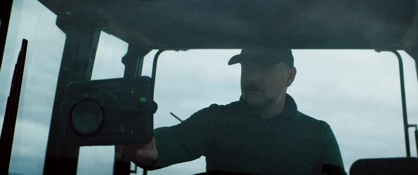 Portrait of 50s Caucasian male farmer using digital tablet while driving tractor through the field. Shot with 2x anamorphic lens