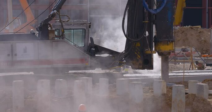 Excavation at a construction site, pile driving machine with rumble and smoke drives piles deep into the ground to ensure the strength of the foundation of the future structure 