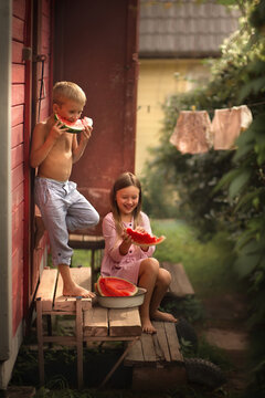 Brother and sister are eating watermelon on the porch in the country in Russia. Image with selective focus and toning