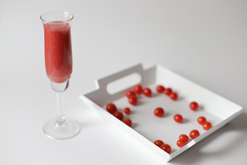 Long glass with fresh red tomato juice and small candy tomatoes on white wooden plate.