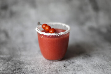 Glass of fresh red tomato juice with salt and metal stick with candy tomatoes on grey background.