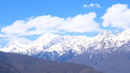 Fototapeta na wymiar picturesque landscape of snow-capped mountains with white clouds on a blue sky on a sunny day at Krasnaya Polyana in Sochi, Russia