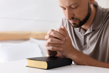 Religious man with Bible praying in bedroom, closeup