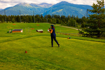 Golfer Teeing Off on Crans Sur Sierre Golf Course with House and Mountain View in Crans Montana in...