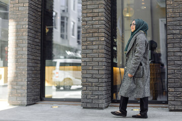 Muslim girl in a green hijab and sunglasses walking on the street