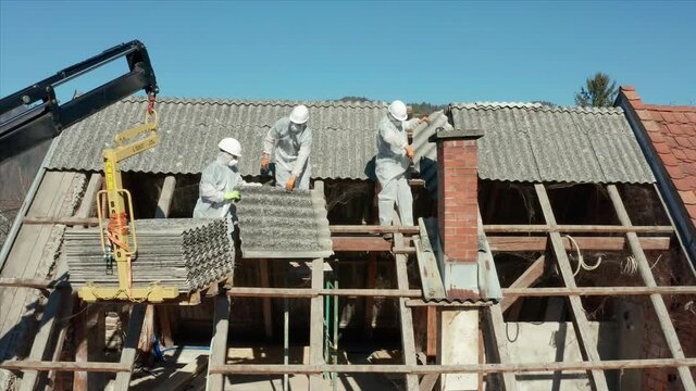 Construction Workers In PPE And Hard Hats Dismantling Roof Tiles Of A Demolished House On A Sunny Day. drone sideways