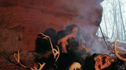 Prehistoric man smoke cigarette in cave on background of snowy forest