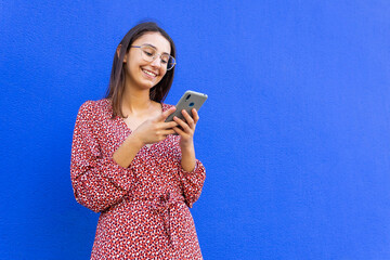 Cheerful female browsing smartphone against blue wall