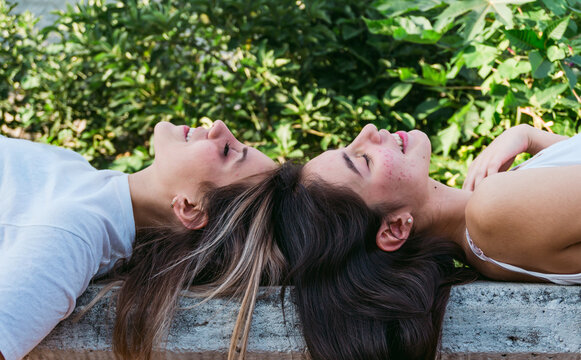 Dreamy girlfriends resting on bench in park