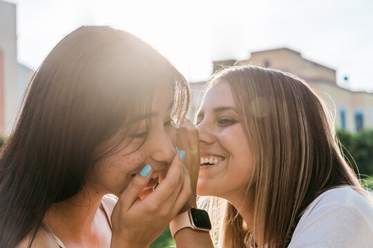 Smiling teenager telling secret to girlfriend on street