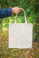 Stylish man hand holding white blank canvas tote shopping bag