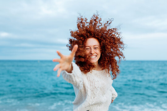 Smiling woman with flying curls reaching hand to camera