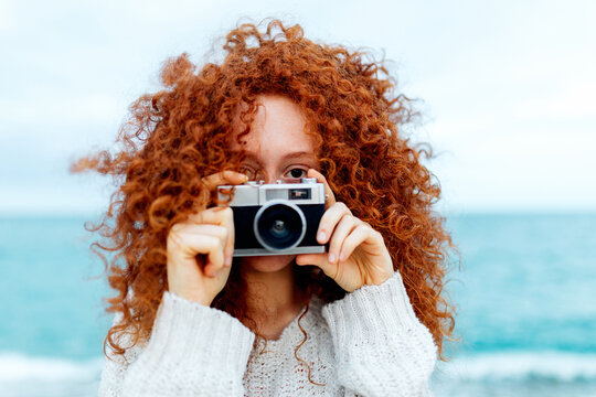 Red haired female taking picture on vintage photo camera