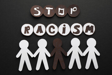 Phrase Stop Racism near white and black paper people on dark background, flat lay