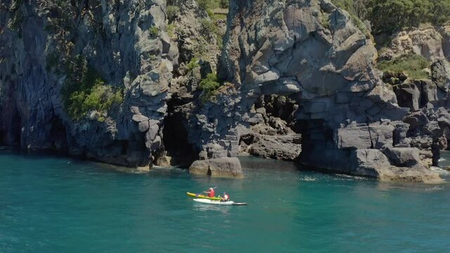 Kayaking beside rock arch on Moutohora Whale Island shore, sunny day
