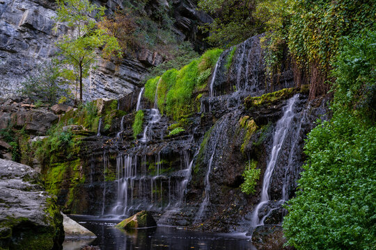 black stone wall with waterfalls falling between the forest and vegetation, rupit catalonia, spain © Diego