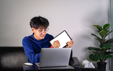 young man using laptop computer and tablet, writing email or message, chatting, shopping, lerning, successful freelancer working online on computer, sitting in modern living room at home.
